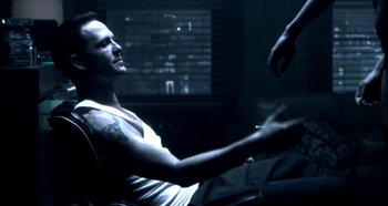 Movie still from “Hellraiser: Hellseeker” (2002), directed by Rick Bota – A man sitting in a chair in a dark room; Medium shot, Over the shoulder angle