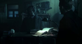 Movie still from “Hellraiser: Hellseeker” (2002), directed by Rick Bota – A person sitting at a table with a book; Medium shot, Over the shoulder angle