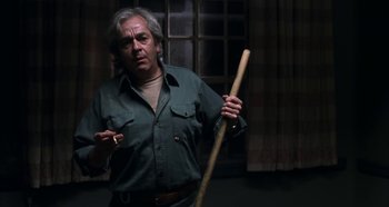 Movie still from “Hellraiser: Hellseeker” (2002), directed by Rick Bota – An older man holding a wooden stick in a room; Medium shot, Low angle