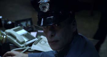 Movie still from “Hellraiser: Hellseeker” (2002), directed by Rick Bota – A man in a police officer's uniform sitting at a desk; Close Up shot, Low angle