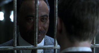 A man in a suit and tie looking at another man in a suit and tie behind bars
