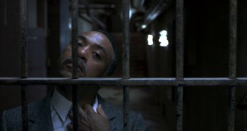 Movie still from “Hellraiser: Hellseeker” (2002), directed by Rick Bota – A man standing behind bars in a jail cell; Close Up shot, High angle