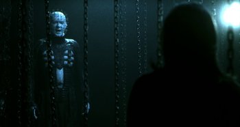 Movie still from “Hellraiser: Hellseeker” (2002), directed by Rick Bota – A man standing in front of a wall with chains hanging from it; Medium shot, Over the shoulder angle