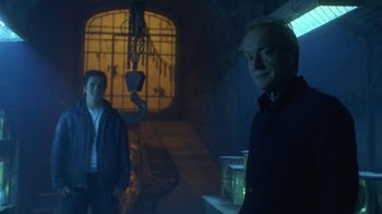 Movie still from “Hellraiser: Hellworld” (2005), directed by Rick Bota – Two people standing in a dark room with smoke coming out of the window; Medium shot, Low angle