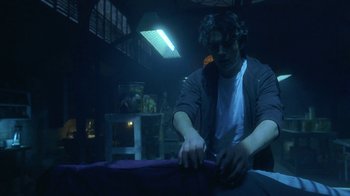 Movie still from “Hellraiser: Hellworld” (2005), directed by Rick Bota – A man is cutting fabric in a dark room; Medium shot, Low angle