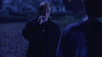 Movie still from “Hellraiser: Hellworld” (2005), directed by Rick Bota – An older man in a black coat is smoking a cigarette; Medium shot, Over the shoulder angle
