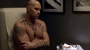 Movie still from “Hellraiser: Inferno” (2000), directed by Scott Derrickson – A bald man sitting in front of a table with his arms crossed; Close Up shot, High angle