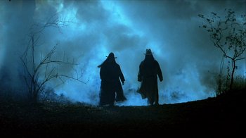 Two men in long coats walking in the fog