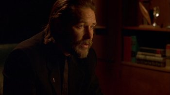 Movie still from “Hellraiser: Inferno” (2000), directed by Scott Derrickson – A man with long hair and a goatee is sitting in a dimly - lit room; Close Up shot, Over the shoulder angle