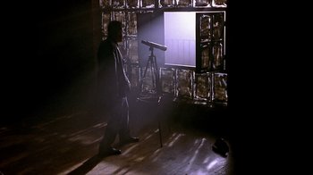 Movie still from “Hellraiser: Inferno” (2000), directed by Scott Derrickson – A man standing in front of a window with a telescope; Wide shot, Low angle