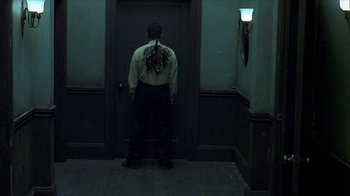 Movie still from “Hellraiser: Inferno” (2000), directed by Scott Derrickson – A man in a yellow shirt is standing in front of a door; Medium shot, Over the shoulder angle