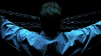 Movie still from “Hellraiser: Inferno” (2000), directed by Scott Derrickson – A man with his arms crossed behind a chain link fence; Close Up shot, Overhead angle