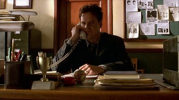 Movie still from “Hellraiser: Inferno” (2000), directed by Scott Derrickson – A man sitting at a table talking on a phone; Medium shot, Low angle