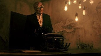 Movie still from “Hellraiser: Judgment” (2018), directed by Gary J. Tunnicliffe – A man in a suit and tie with a typewriter in front of him; Medium shot, Low angle