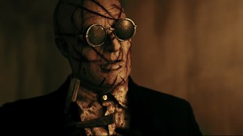 Movie still from “Hellraiser: Judgment” (2018), directed by Gary J. Tunnicliffe – A man in a suit and tie wearing sunglasses; Close Up shot, Low angle