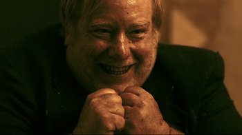 Movie still from “Hellraiser: Judgment” (2018), directed by Gary J. Tunnicliffe – An older man smiling with his hands on his chin; Close Up shot, High angle