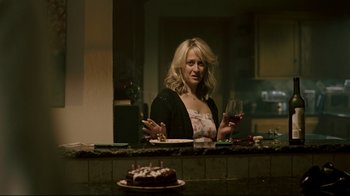 Movie still from “Hellraiser: Judgment” (2018), directed by Gary J. Tunnicliffe – A woman sitting at a table with a cake and a glass of wine in front of her; Medium shot, Over the shoulder angle