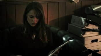 Movie still from “Hellraiser: Judgment” (2018), directed by Gary J. Tunnicliffe – A woman sitting on a couch looking at a book; Close Up shot, Over the shoulder angle
