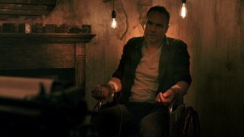 Movie still from “Hellraiser: Judgment” (2018), directed by Gary J. Tunnicliffe – A man sitting in a chair in front of a fire place; Medium shot, Low angle