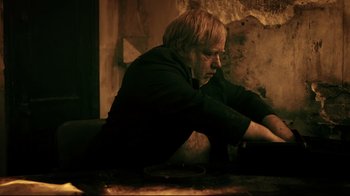 Movie still from “Hellraiser: Judgment” (2018), directed by Gary J. Tunnicliffe – A man sitting on the ground in front of a stone wall; Medium shot, High angle