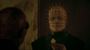 Movie still from “Hellraiser: Judgment” (2018), directed by Gary J. Tunnicliffe – A man with a pinhead mask is looking at a piece of paper in front of him; Close Up shot, Over the shoulder angle