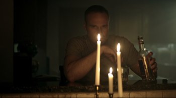Movie still from “Hellraiser: Judgment” (2018), directed by Gary J. Tunnicliffe – A man sitting in front of a table with lit candles; Medium shot, Low angle