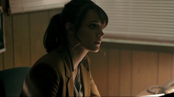 Movie still from “Hellraiser: Judgment” (2018), directed by Gary J. Tunnicliffe – A woman with a ponytail is sitting in a dimly lit room; Close Up shot, Over the shoulder angle