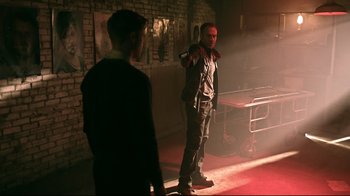 Movie still from “Hellraiser: Judgment” (2018), directed by Gary J. Tunnicliffe – A man standing next to another man on a stage; Wide shot, Over the shoulder angle