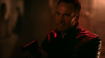 Movie still from “Hellraiser: Judgment” (2018), directed by Gary J. Tunnicliffe – A man holding a gun while wearing a black jacket; Close Up shot, Over the shoulder angle