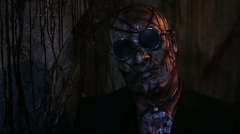 Movie still from “Hellraiser: Judgment” (2018), directed by Gary J. Tunnicliffe – A man in a suit and sunglasses with a face covered in blood; Close Up shot, Low angle