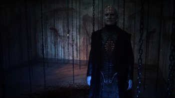 Movie still from “Hellraiser: Judgment” (2018), directed by Gary J. Tunnicliffe – A man in a black outfit standing next to chains; Medium shot, Low angle