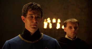 Movie still from “Henry V” (1989), directed by Kenneth Branagh – A man standing next to another man in front of candles; Close Up shot, Over the shoulder angle