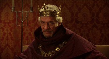 Movie still from “Henry V” (1989), directed by Kenneth Branagh – An older man wearing a crown and a red robe; Medium shot, Over the shoulder angle