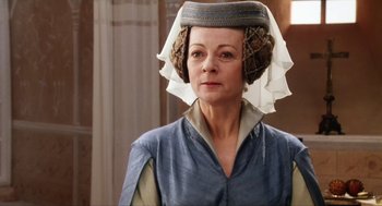 Movie still from “Henry V” (1989), directed by Kenneth Branagh – An older woman wearing a hat and a blue dress; Close Up shot, Over the shoulder angle