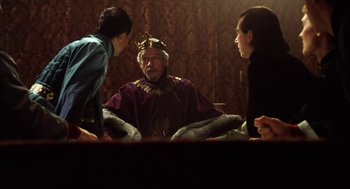 Movie still from “Henry V” (1989), directed by Kenneth Branagh – A man in a crown sitting next to two other people; Medium shot, Over the shoulder angle