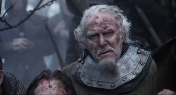 Movie still from “Henry V” (1989), directed by Kenneth Branagh – An old man with a beard and a helmet on; Close Up shot, Over the shoulder angle