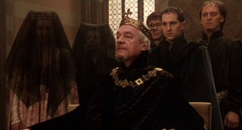 Movie still from “Henry V” (1989), directed by Kenneth Branagh – A group of people in a room with a man wearing a crown; Medium shot, High angle