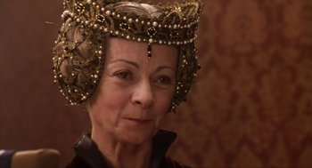 Movie still from “Henry V” (1989), directed by Kenneth Branagh – An older woman wearing a crown with pearls on her head; Close Up shot, Over the shoulder angle