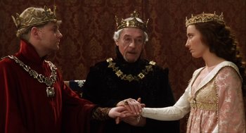 Movie still from “Henry V” (1989), directed by Kenneth Branagh – A man wearing a crown and holding hands with two other people; Medium shot, High angle