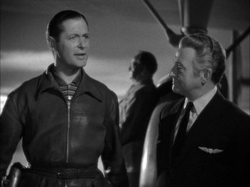 Movie still from “Here Comes Mr. Jordan” (1941), directed by Alexander Hall – A man in a leather jacket standing next to another man in a suit; Medium shot, Over the shoulder angle
