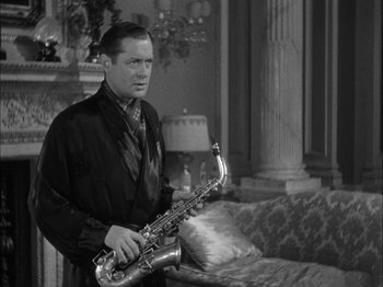 Movie still from “Here Comes Mr. Jordan” (1941), directed by Alexander Hall – A man holding a saxophone while standing next to a couch; Medium shot, High angle