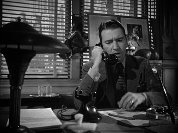 Movie still from “Here Comes Mr. Jordan” (1941), directed by Alexander Hall – A man sitting at a desk talking on a phone; Medium shot, Low angle
