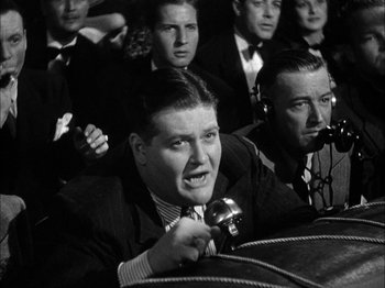 Movie still from “Here Comes Mr. Jordan” (1941), directed by Alexander Hall – A man is speaking at a microphone in front of a group of people; Medium shot, Low angle