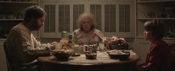 Movie still from “Hesher” (2010), directed by Spencer Susser – An older woman sitting at a table with a lot of food; Medium shot, High angle