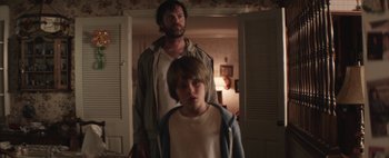 Movie still from “Hesher” (2010), directed by Spencer Susser – A man standing next to a young boy in a room; Medium shot, Over the shoulder angle
