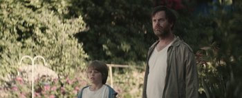 Movie still from “Hesher” (2010), directed by Spencer Susser – A man standing next to a young boy in front of bushes; Medium shot, Over the shoulder angle