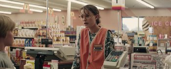 Movie still from “Hesher” (2010), directed by Spencer Susser – A woman in an orange vest stands at a cash register; Medium shot, Over the shoulder angle