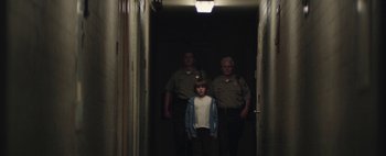 Movie still from “Hesher” (2010), directed by Spencer Susser – A young boy standing between two police officers in a hallway; Wide shot, Low angle