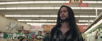 Movie still from “Hesher” (2010), directed by Spencer Susser – A man with long black hair and a plaid shirt in a grocery store; Close Up shot, Over the shoulder angle