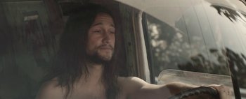 Movie still from “Hesher” (2010), directed by Spencer Susser – A man with long black hair sitting in a car holding a drink; Close Up shot, Over the shoulder angle